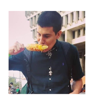 José is eating a corn on the cob in front of a building. He is wearing a dark blue shirt and has a buzzed haircut (dark hair)