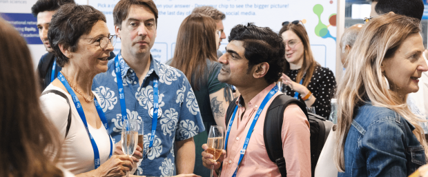 3 people discuss in a crowd. they hold a glass of bubbly wine. on the left a person with a white top, on the right, a person with a salmon shirt. in the middle someone with a blue shirt with white prints.